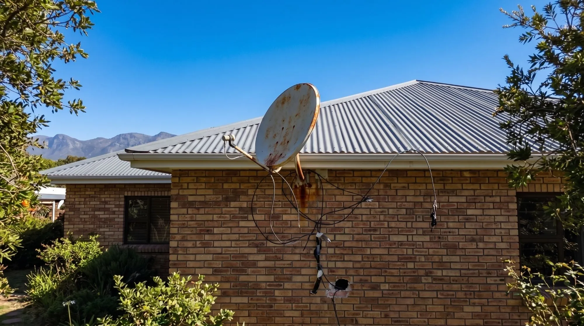 Before: a rusted satellite dish on a brick house with loose cables hanging down the wall and a hole broken into the brickwork